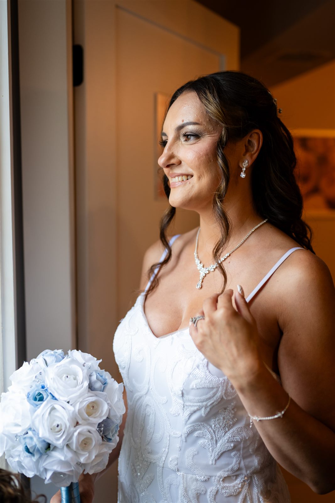 Bride smiling at the window with her blue and white bouquet before the ceremony
