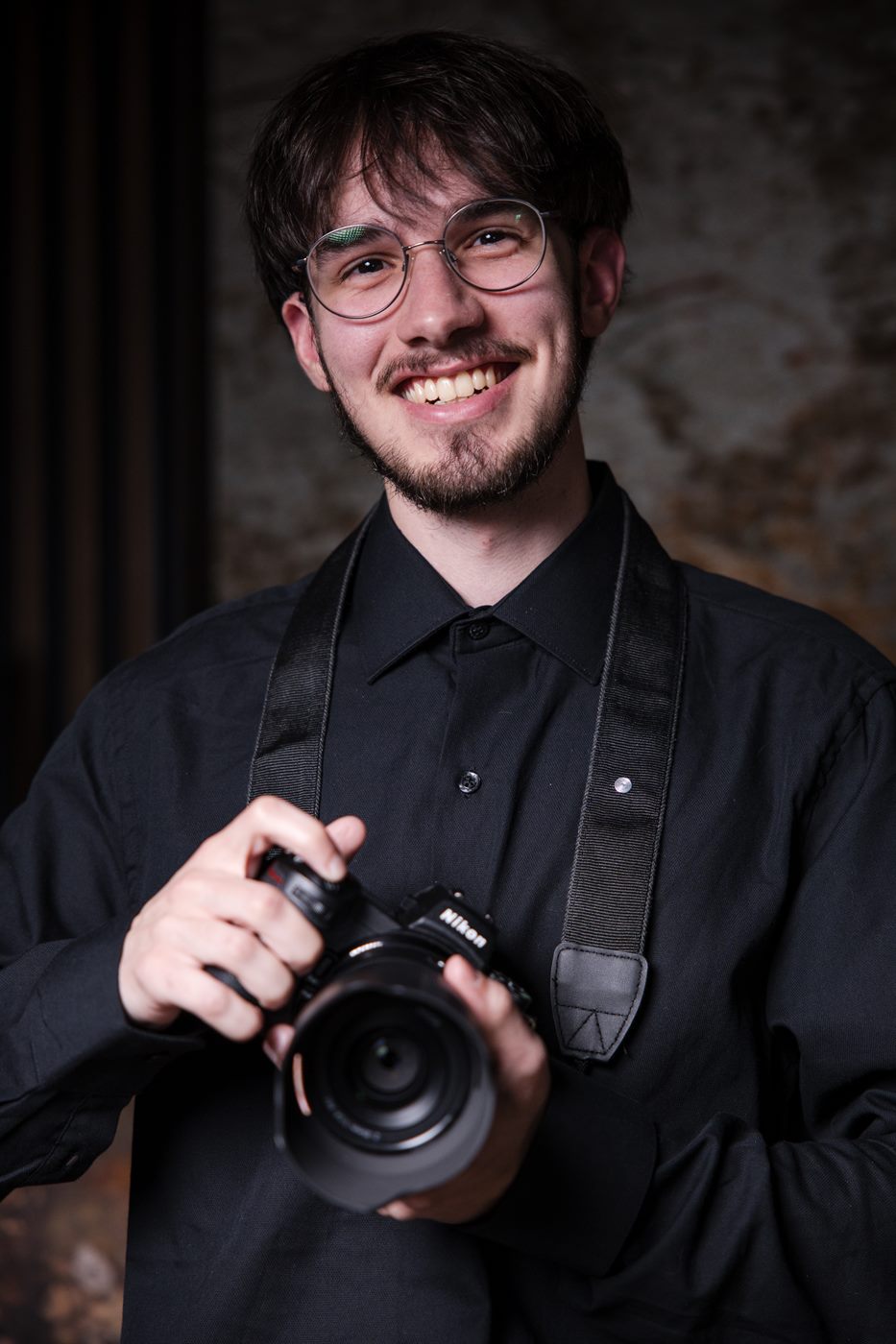 Nick Schluth smiling with his Nikon camera around his neck