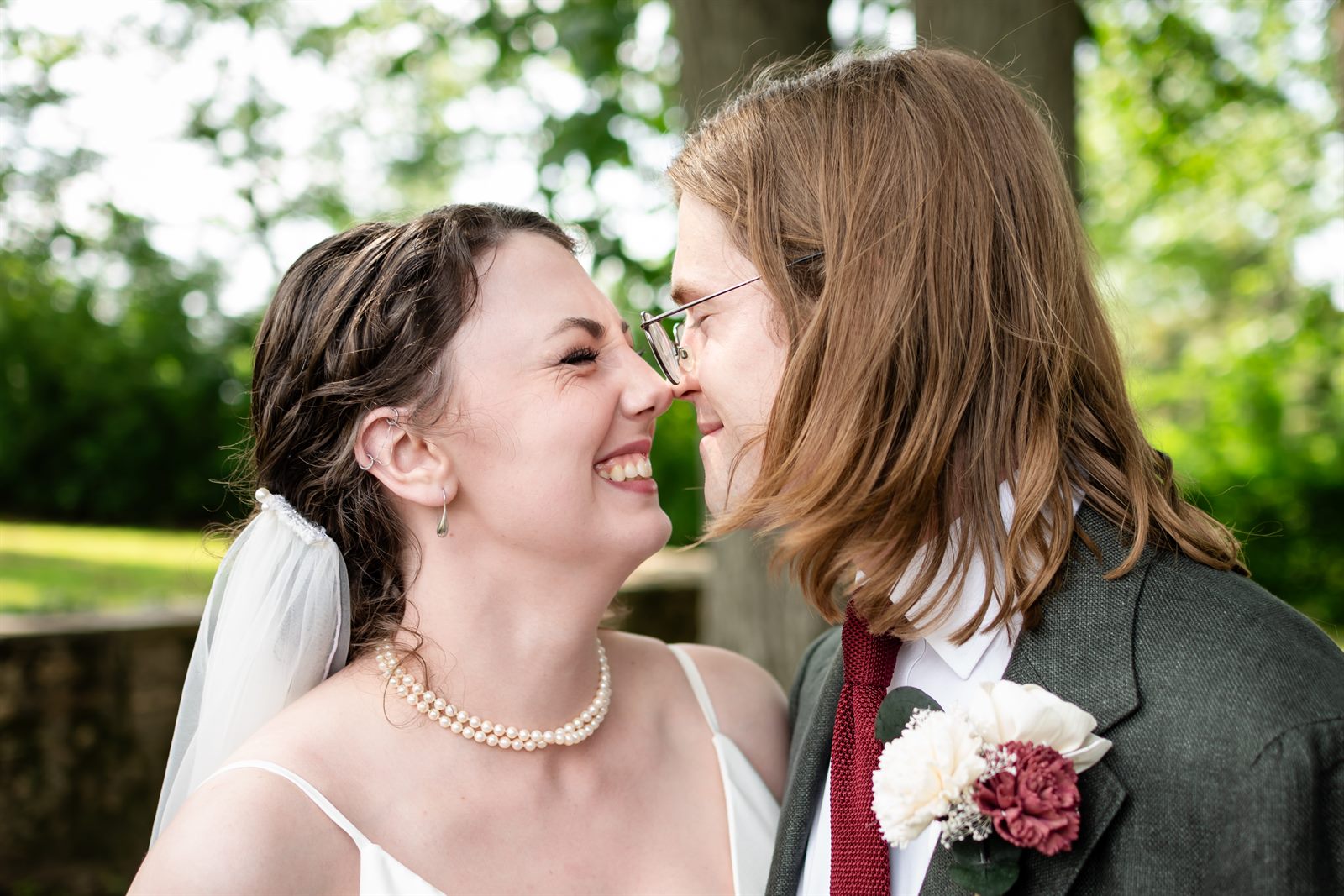 Bride and groom smiling nose to nose under the trees